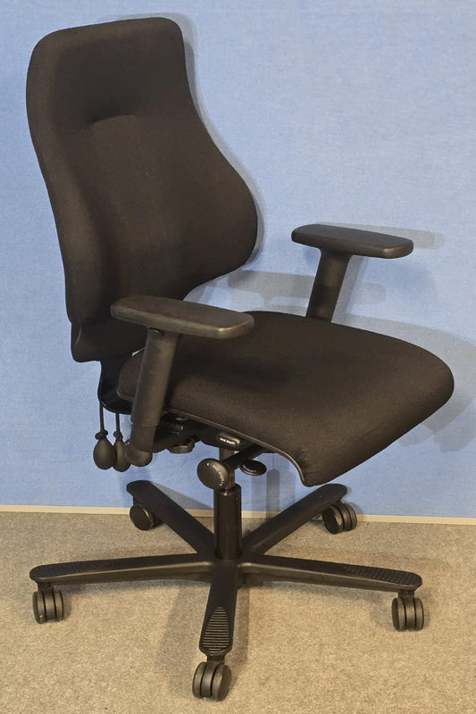 Black office chair with adjustable arms on a grey floor and light blue wall background