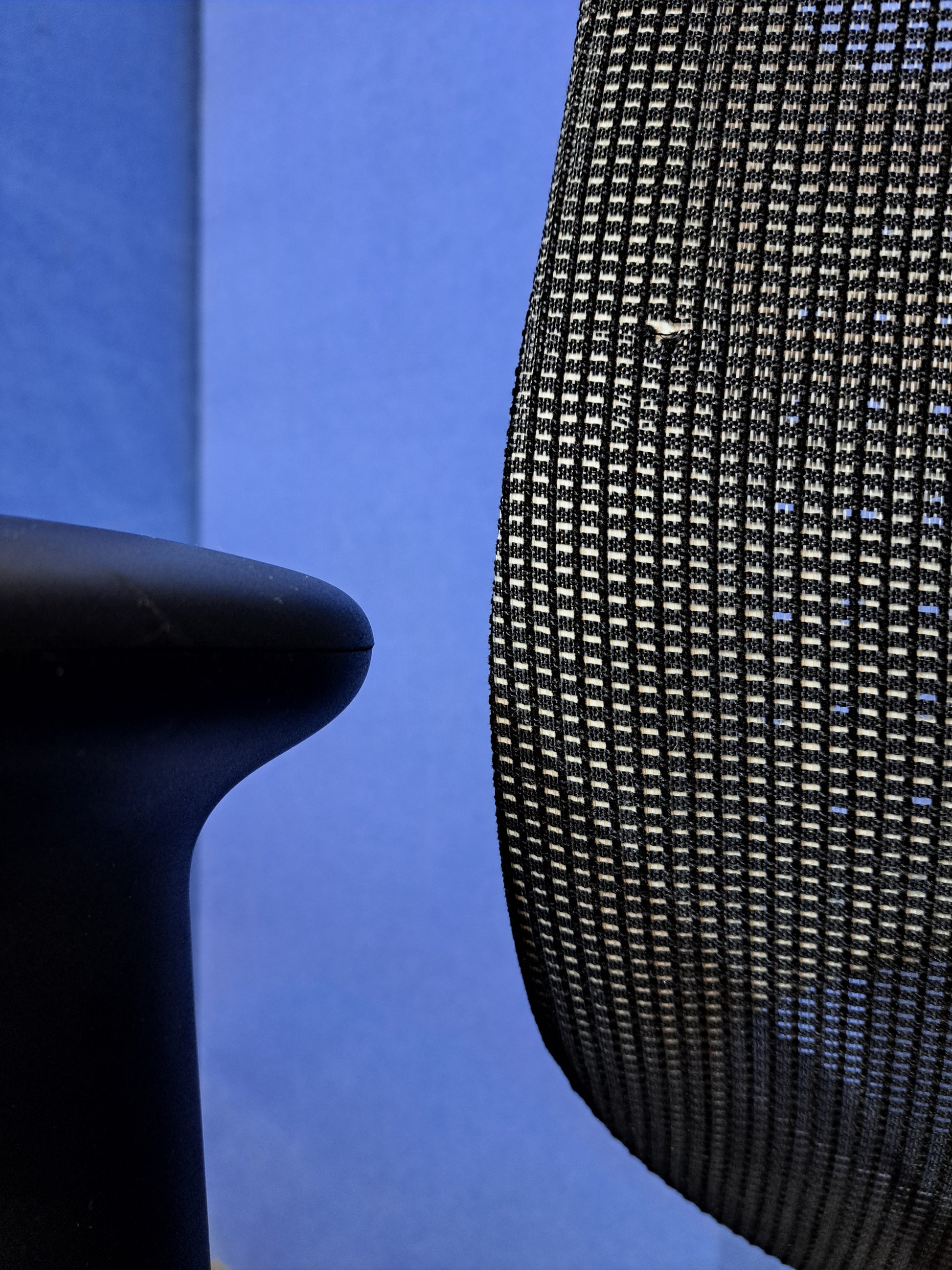 Grey mesh back office chair on a blue wall and grey carpet