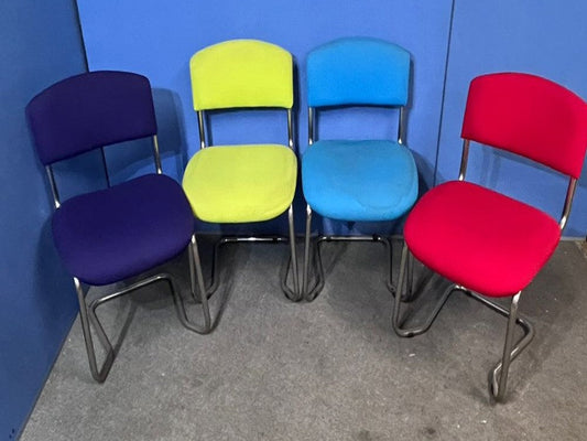 Four colorful chairs in purple, yellow, blue, and red against a blue wall.