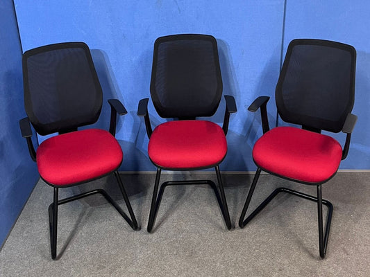 Three office chairs with red seats and black mesh backs against a blue wall.