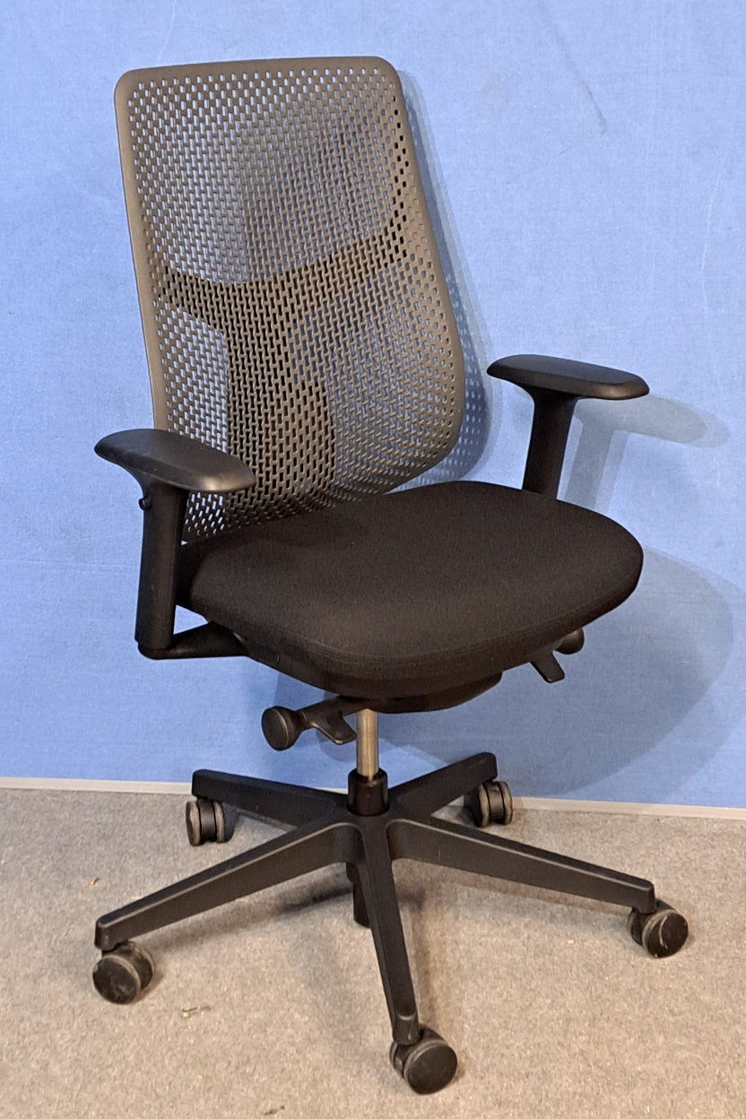 Black office chair with mesh backrest against a blue wall.