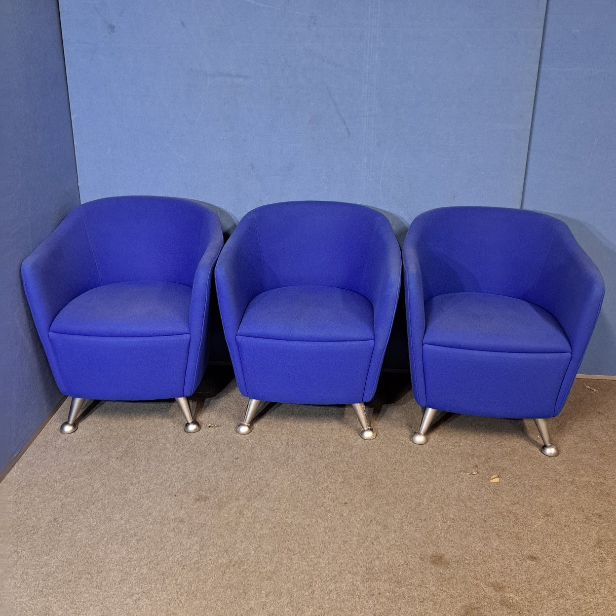 Three blue chairs with silver legs on a blue wall and grey floor