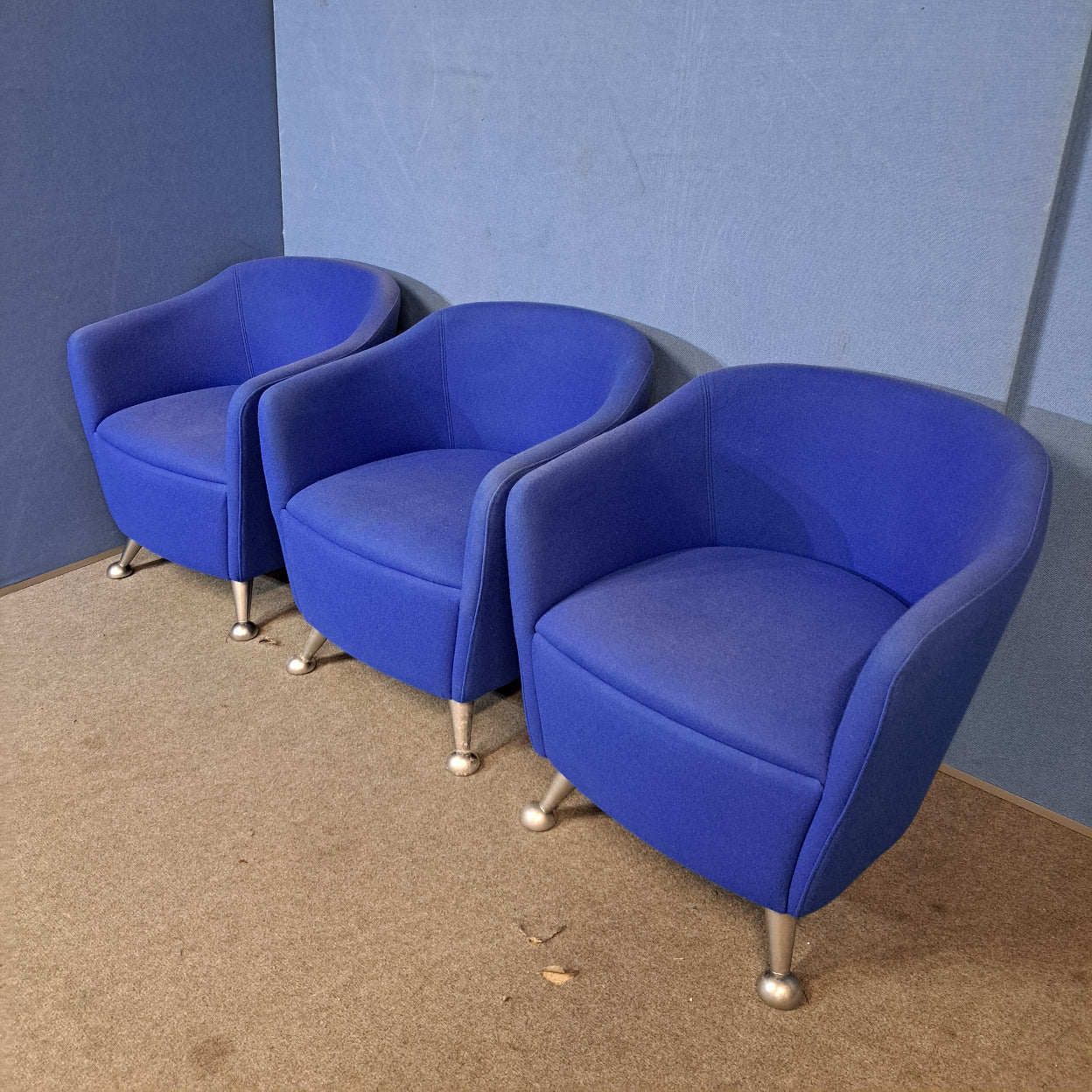 Three blue chairs with silver legs on a blue wall and grey floor