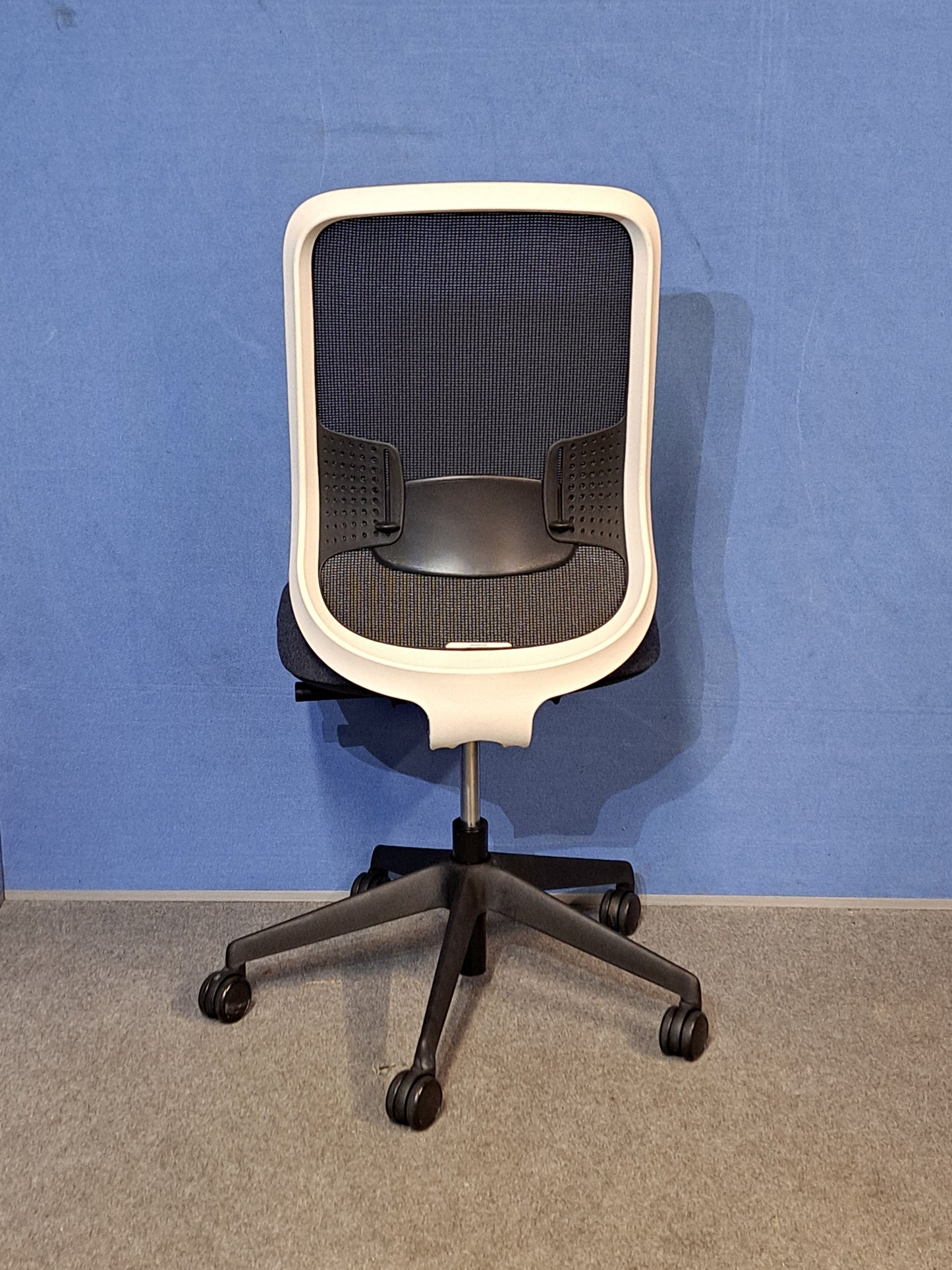 Grey / black office chair on a blue wall and grey carpet