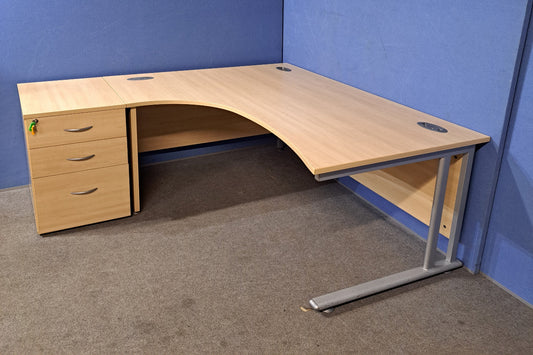 Wooden L-shaped desk with drawers against a blue wall.