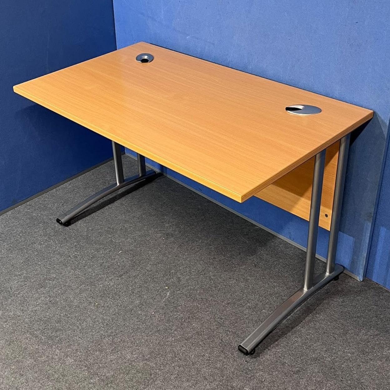 Beech straight desk against a blue wall and grey floor