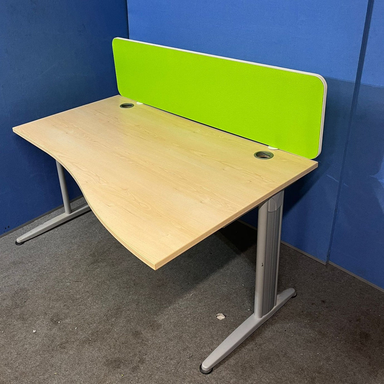 Wooden desk with a green partition against a blue wall.