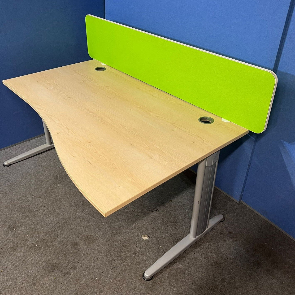 Wooden desk with a green partition against a blue wall.