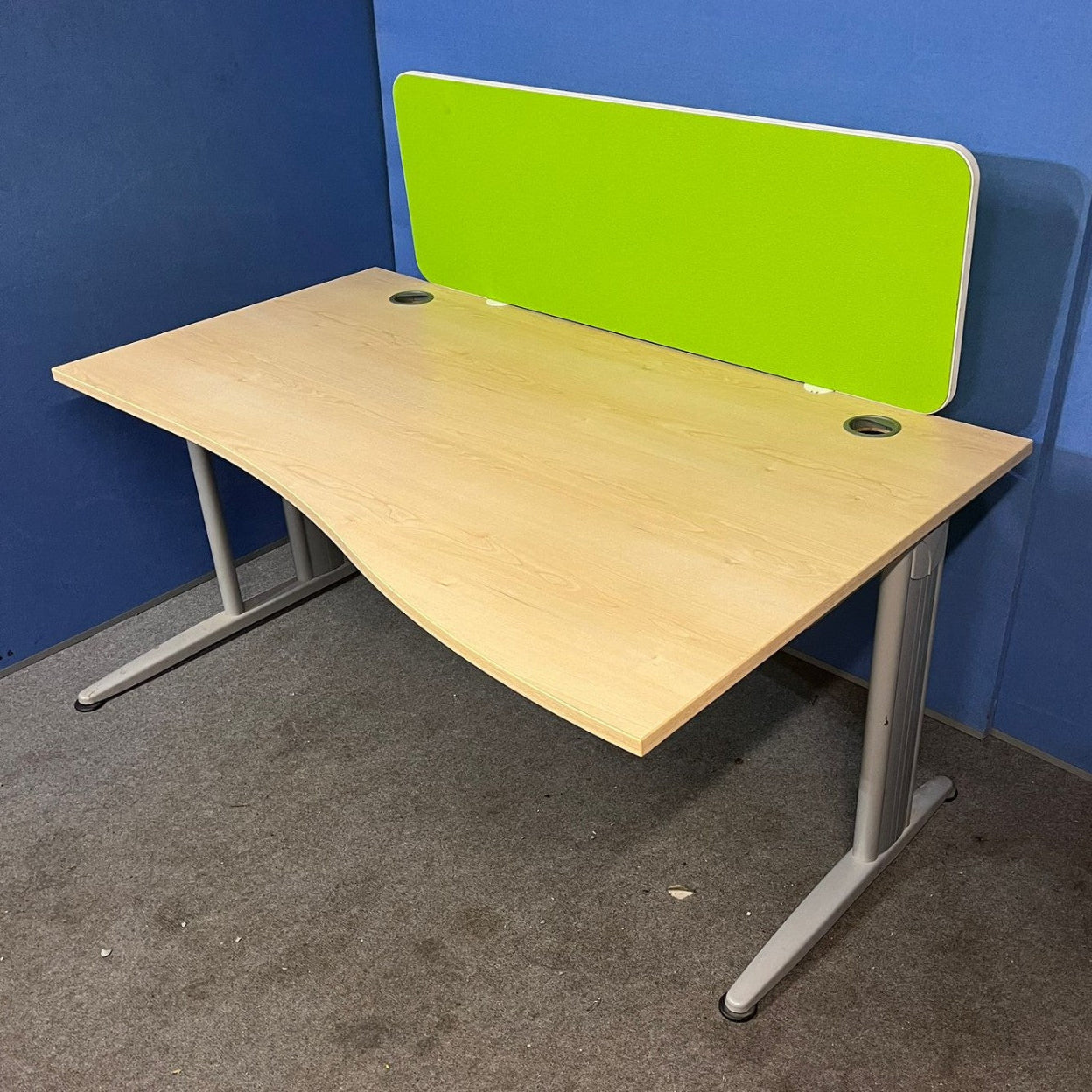 Wooden desk with a green partition against a blue wall.
