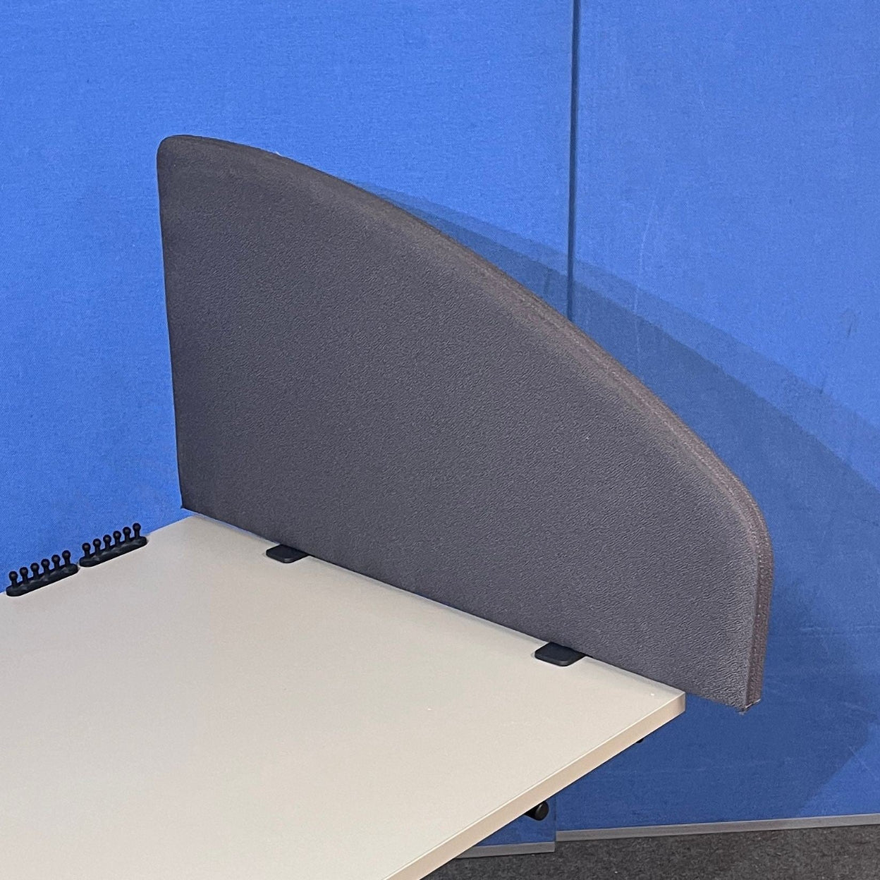 Gray fabric desk screen attached to a beige desk against a blue wall.