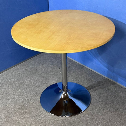 Round wooden table with a metallic base against a blue wall.