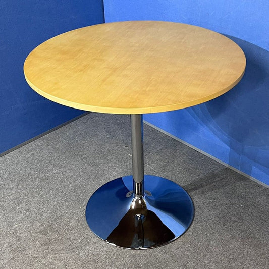 Round wooden table with a metallic base against a blue wall.