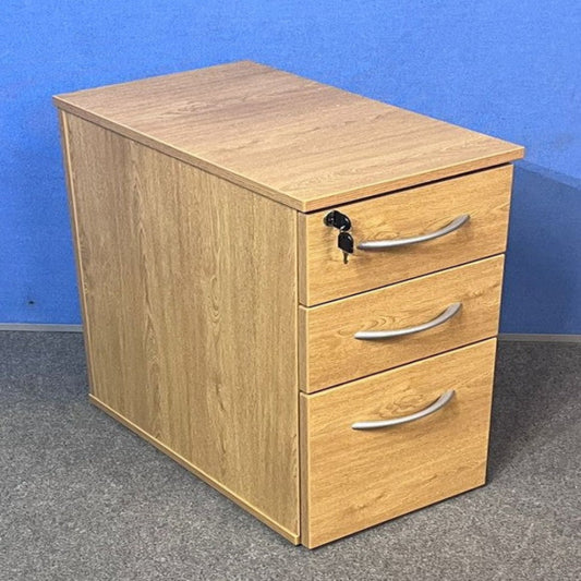Wooden pedestal with three drawers against a blue wall.