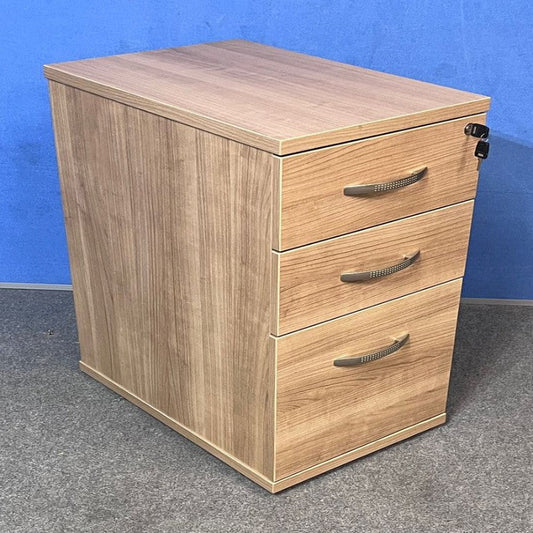 Wooden pedestal with three drawers on a grey floor against a blue wall