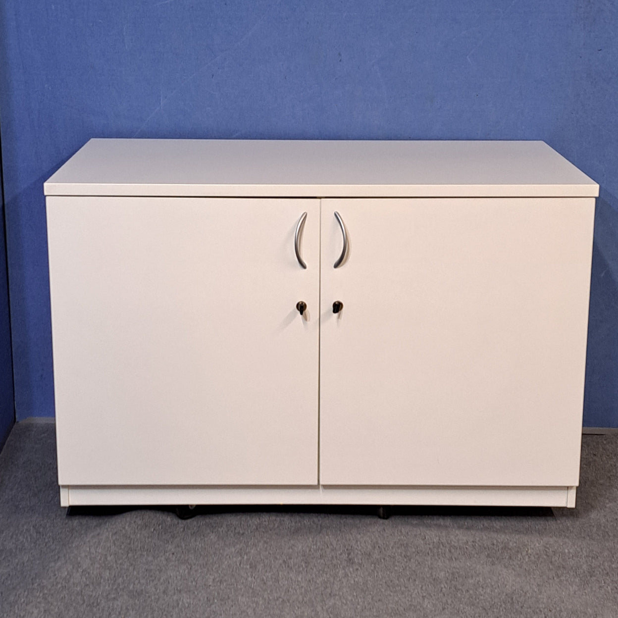 White cupboard on a blue wall and grey carpet